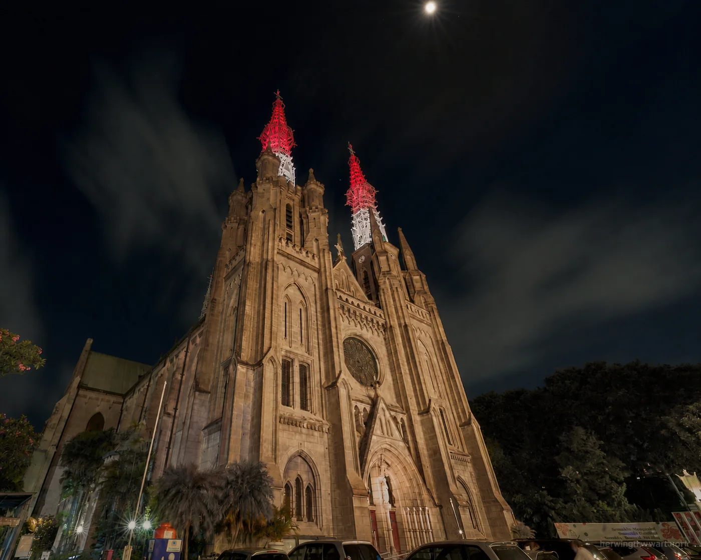 Jakarta Cathedral's twin openwork spires shown in the Merah Putih scene, red across the upper lattice and white below, over the warm white Neo-Gothic facade